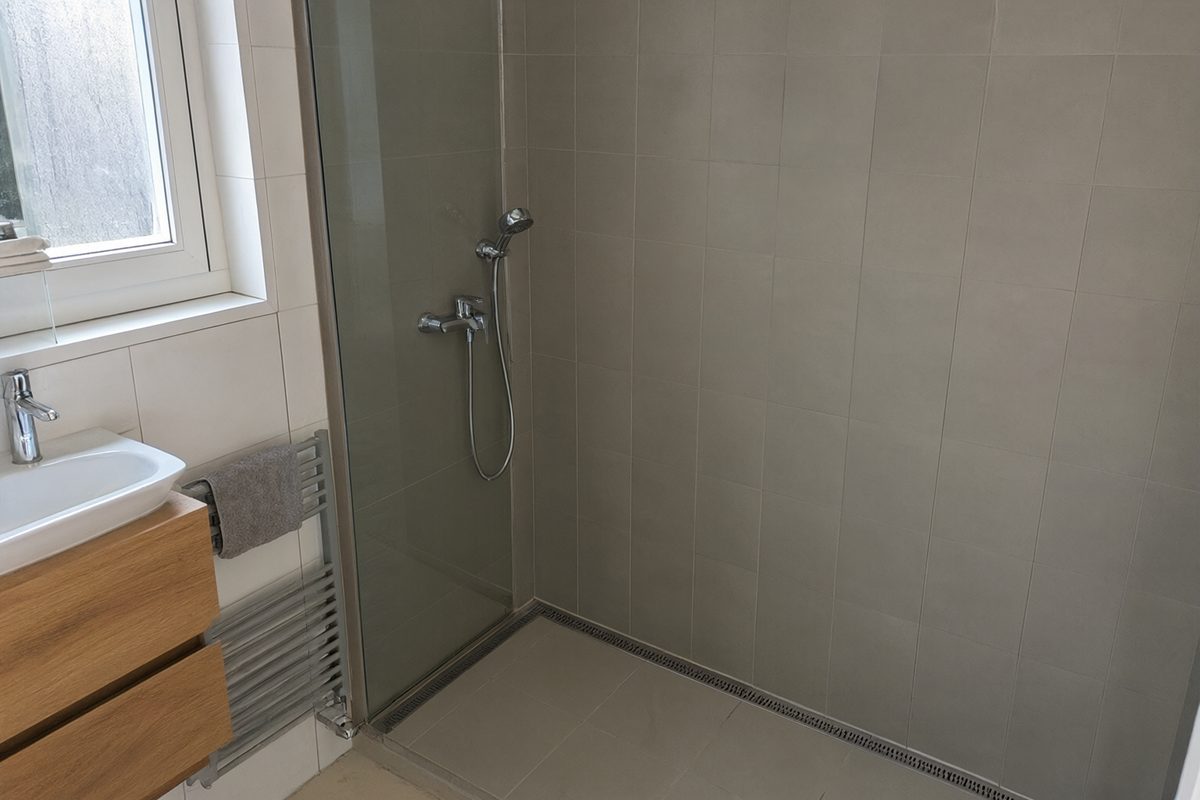 Douche de plain-pied à paroi fixe à côté d'un meuble vasque en bois
